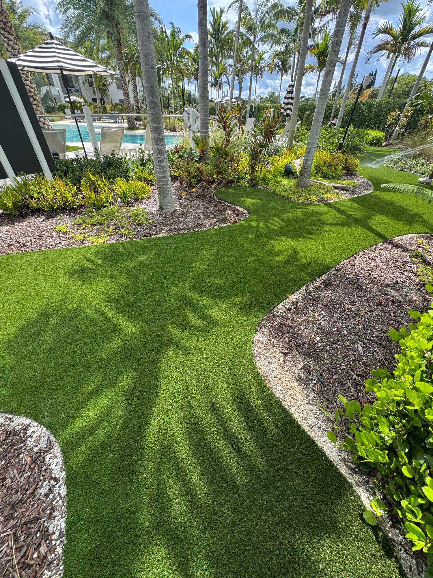 Curved artificial turf path installed through tropical landscaping beside a pool